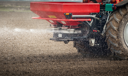 Tractor in a field spreading liquid fertilizer, close-up of rear and red attachment spraying droplets onto the soil. Vibrant scene of agriculture in action.