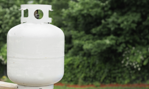 A white propane tank stands outdoors against a lush green, leafy background, suggesting a serene and natural setting.